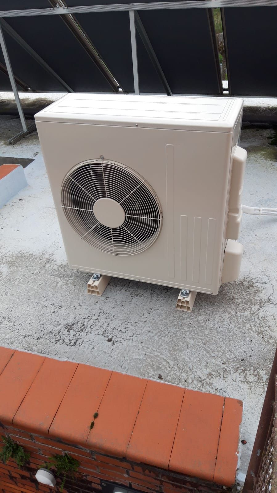 Un acondicionador de aire blanco está colocado sobre una superficie de hormigón al lado de una pared de ladrillos.