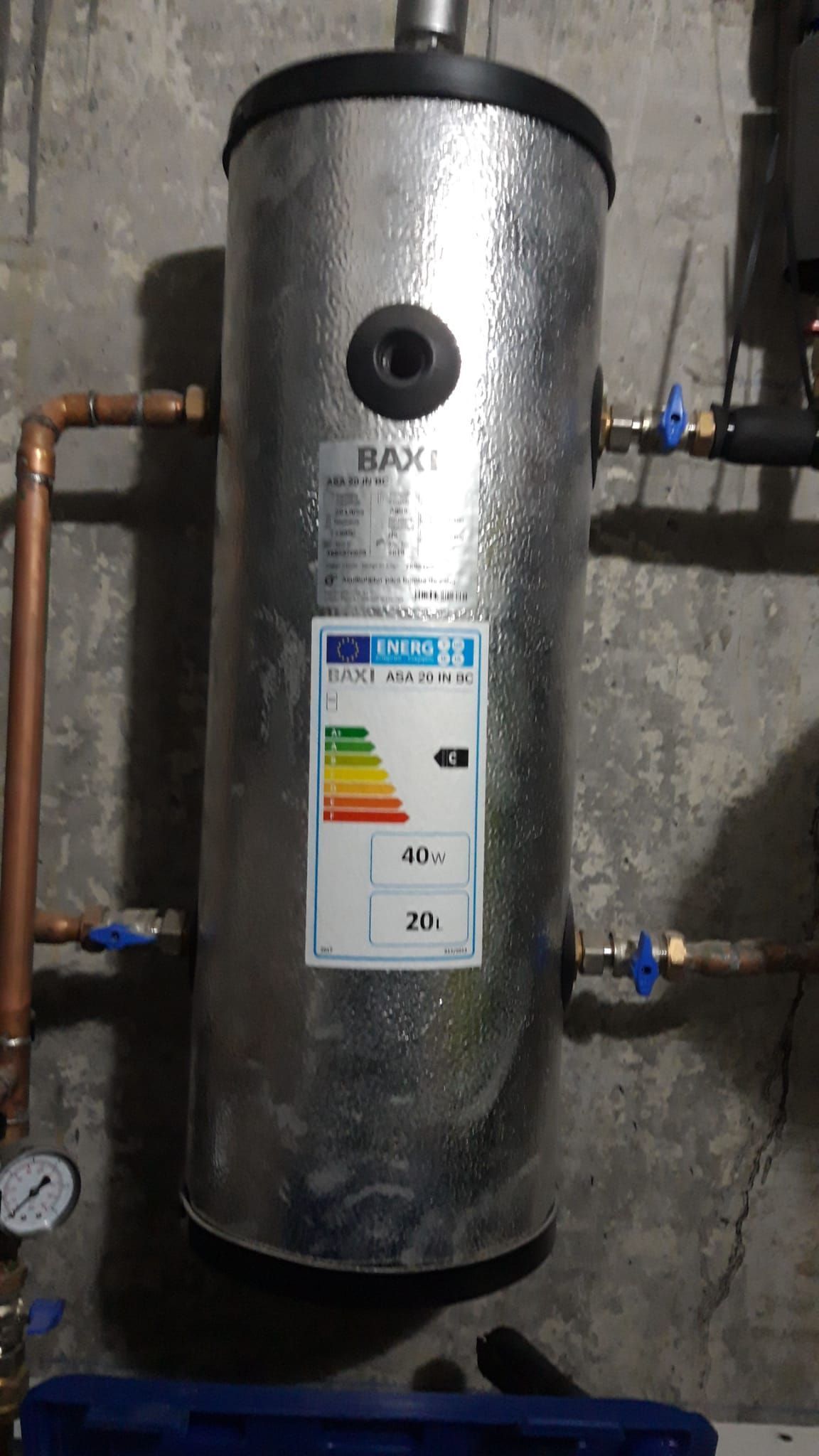 Un calentador de agua de acero inoxidable con una etiqueta está colgado en una pared.