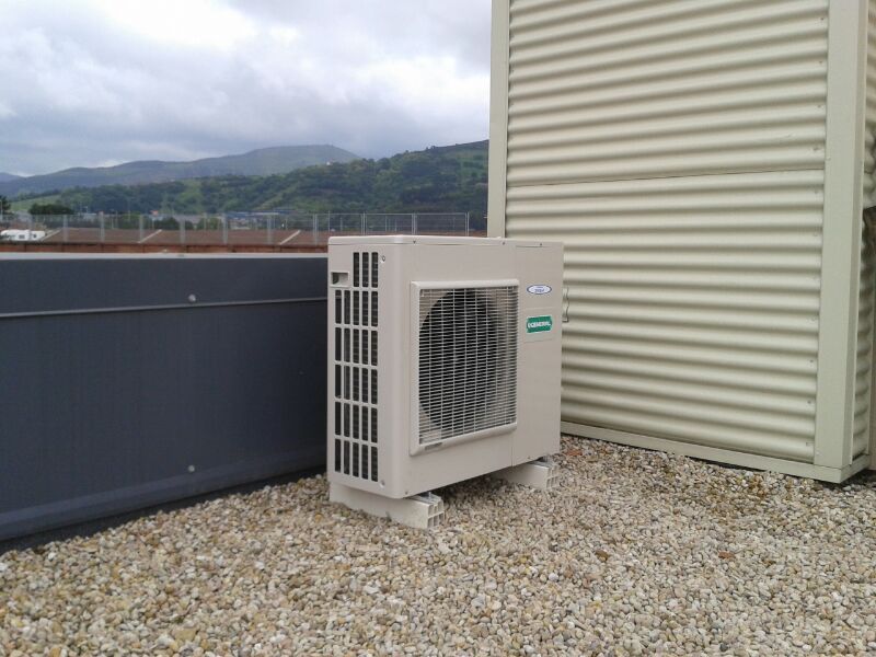 Un acondicionador de aire blanco está situado encima de un techo de grava al lado de un edificio.