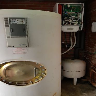 Un calentador de agua blanco está ubicado en una habitación al lado de una pared de ladrillos.