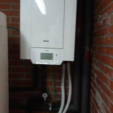 Una caldera blanca está colgada en una pared de ladrillos al lado de un tanque de agua.