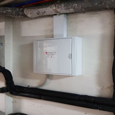 Una caja blanca está colgada en una pared al lado de unas tuberías.