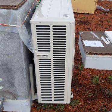 Un acondicionador de aire blanco está en el suelo al lado de una pared.