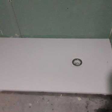 Un plato de ducha blanco con un agujero en el medio en un baño.