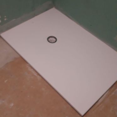 Un plato de ducha blanco está sobre el suelo en un baño.
