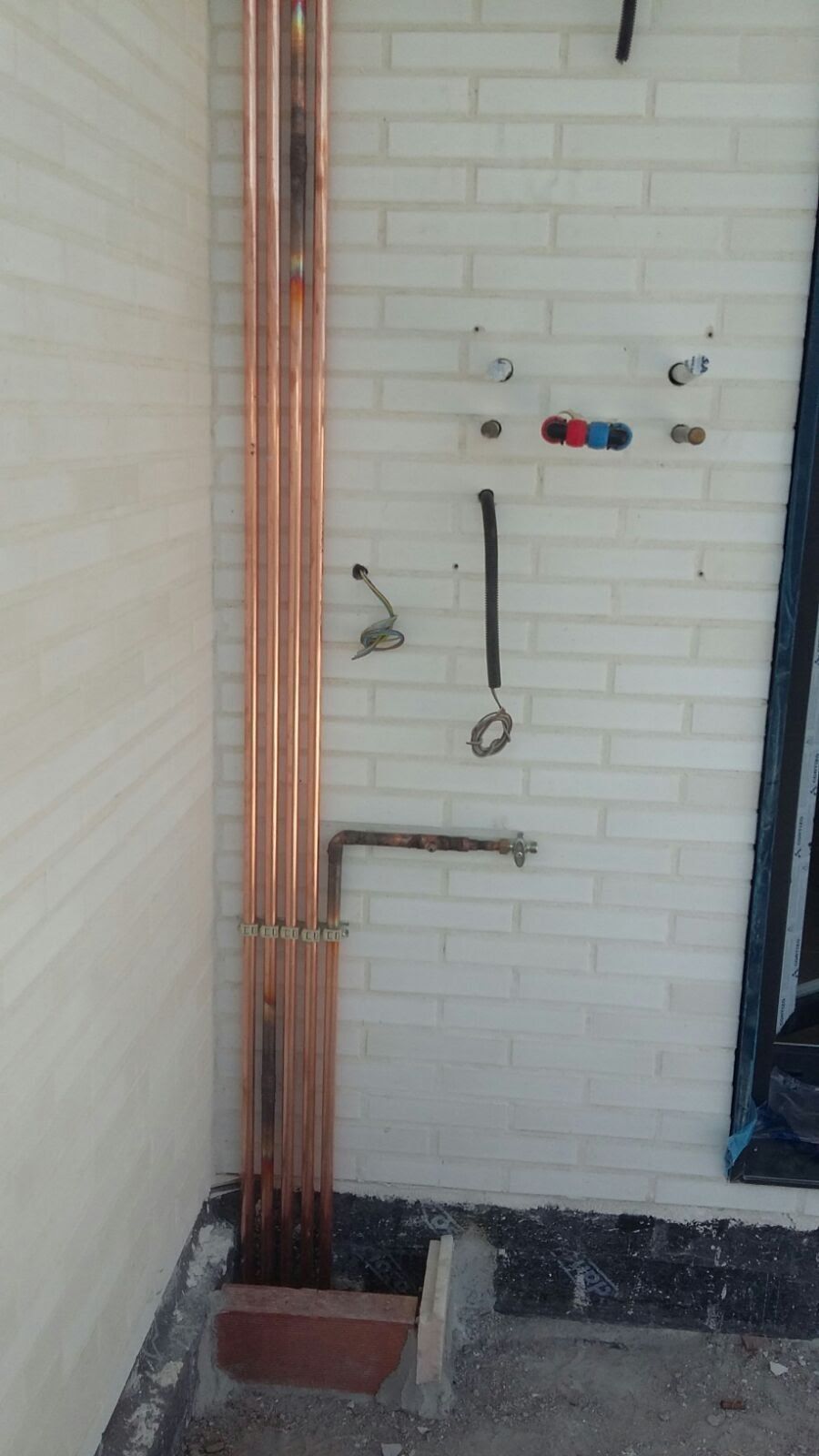 Se están instalando tuberías de cobre en una pared de ladrillo blanco.