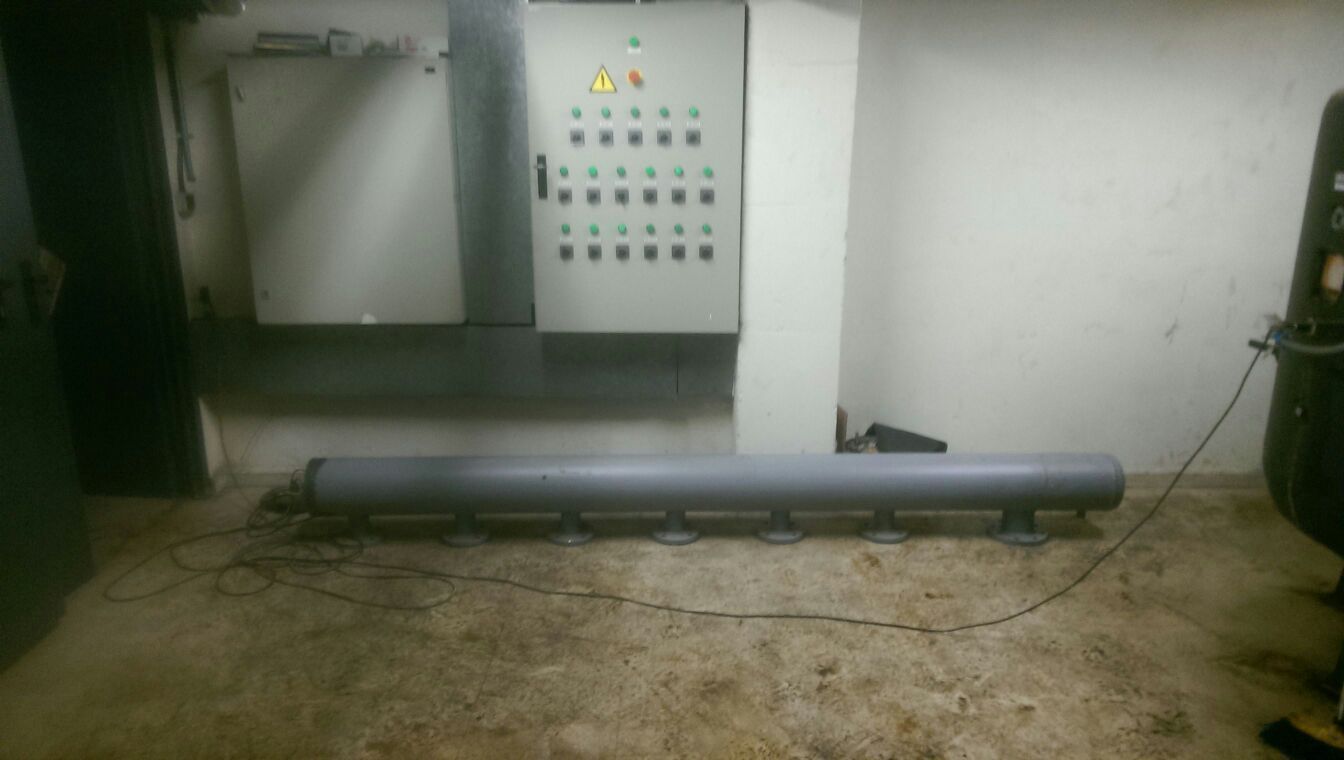 Hay una tubería grande en el suelo en una habitación al lado de un panel de control.