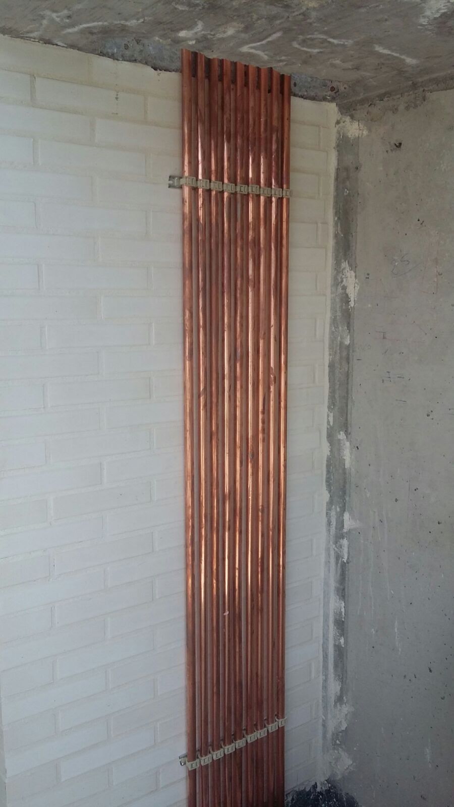 Se están instalando tuberías de cobre en una pared de ladrillo blanco.