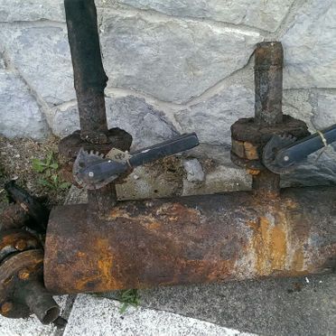 Una tubería oxidada está en el suelo junto a una pared de ladrillos.