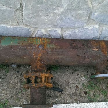 Una tubería oxidada está en el suelo junto a una pared de ladrillos.