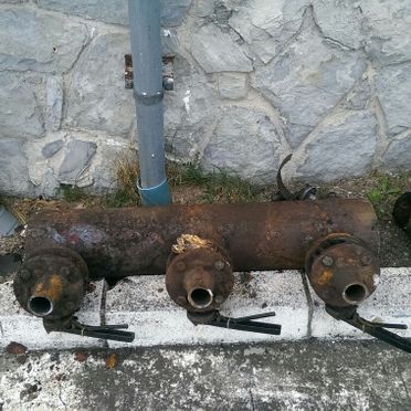 Una tubería oxidada se encuentra en una acera al lado de un muro de piedra.