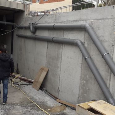 Un hombre está parado frente a una pared de la que salen tuberías.