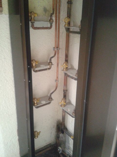 Un rincón de una habitación con tubos de cobre y estantes.