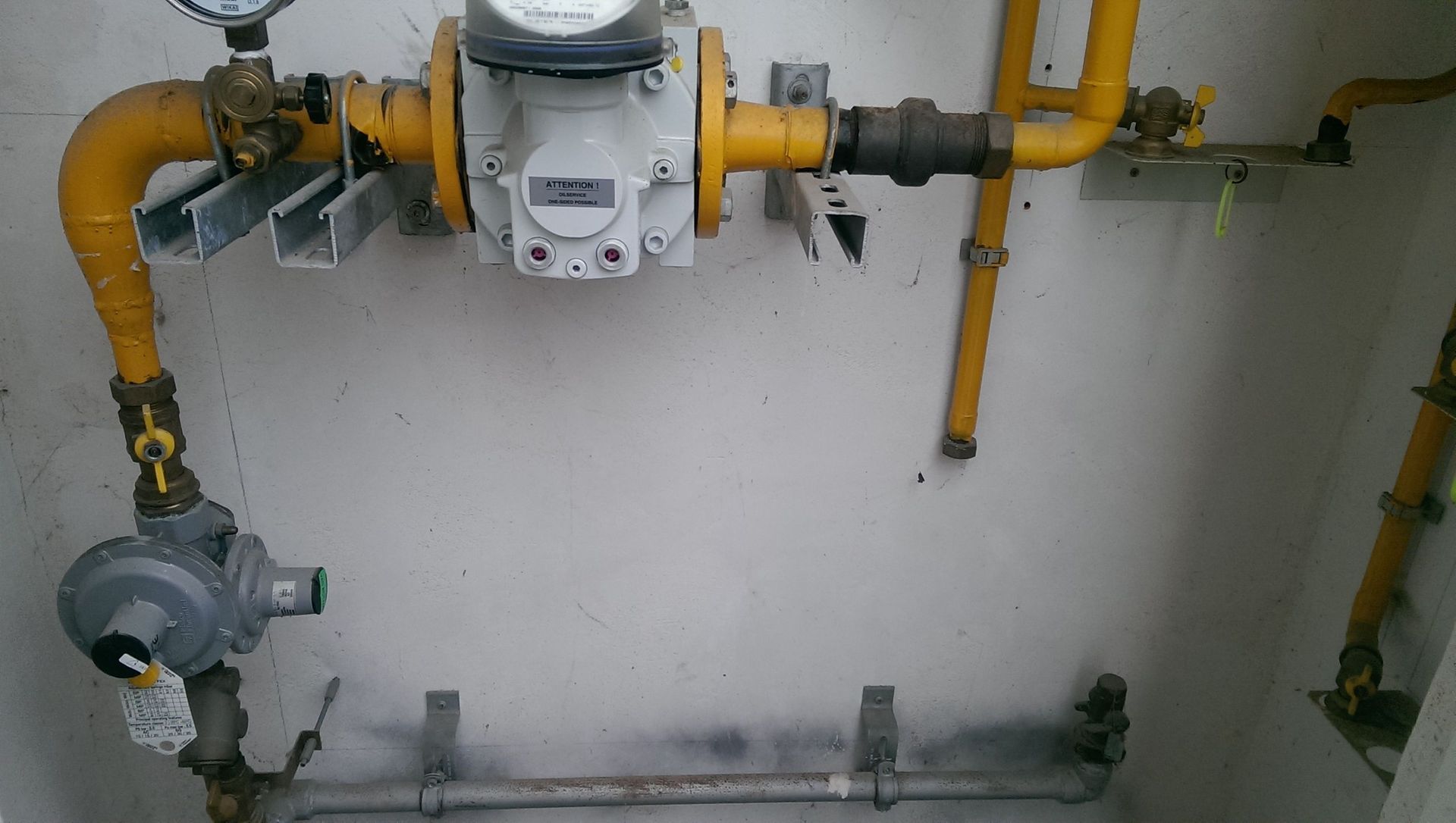 Un medidor de gas está conectado a una tubería amarilla en una habitación.