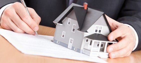 Una persona sostiene una maqueta de casa y escribe en un trozo de papel.