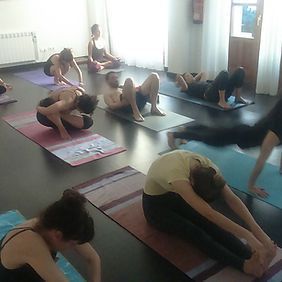 Personas en una clase de yoga sobre colchonetas, estirándose y practicando posturas en una sala con luz natural.