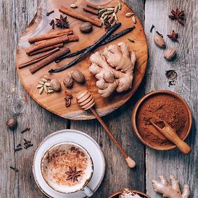 Especias dispuestas sobre madera con una taza de chai. Se aprecian canela, nuez moscada, jengibre y una cuchara de miel.