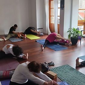 Personas estirándose en una clase de yoga sobre colchonetas en una sala luminosa con suelo de madera.