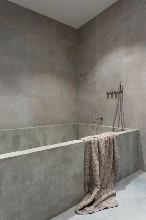 Ein Badezimmer mit einer Betonbadewanne und einem Handtuch auf dem Boden.