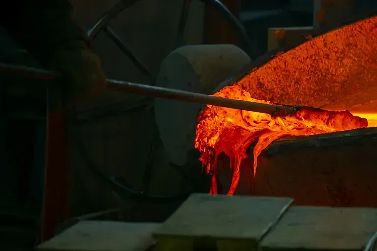 Un primer plano de una persona vertiendo metal fundido en un horno.