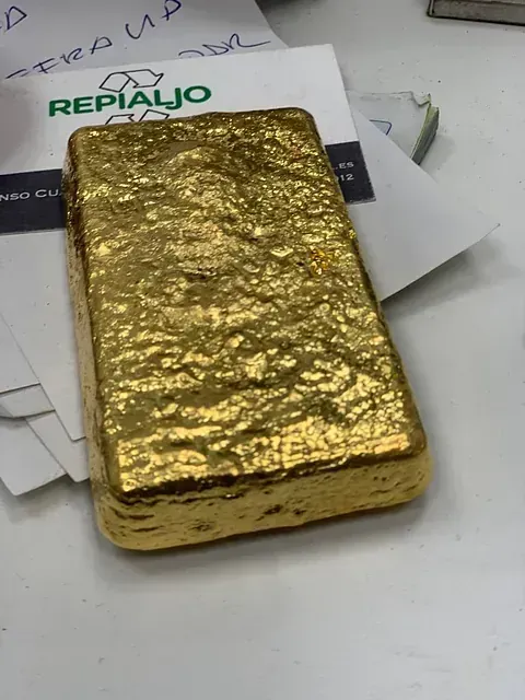 Una barra de oro está sobre una mesa junto a una tarjeta de repiaio