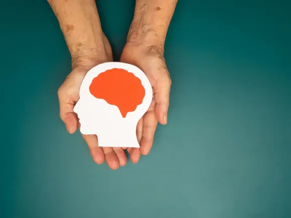 Manos sosteniendo una silueta blanca de una cabeza con un cerebro rojo sobre un fondo verde azulado.