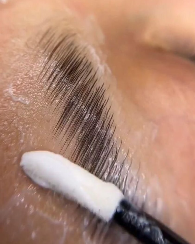 Primer plano de los pelos de las cejas con aplicación de crema con un hisopo de algodón.