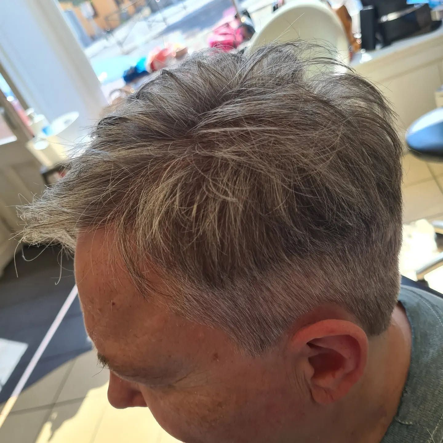Une personne aux cheveux gris courts assise dans un fauteuil de salon de coiffure.