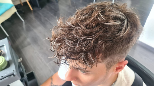Coupe de cheveux bruns bouclés sur un fauteuil de salon, avec les côtés rasés et le dessus texturé.