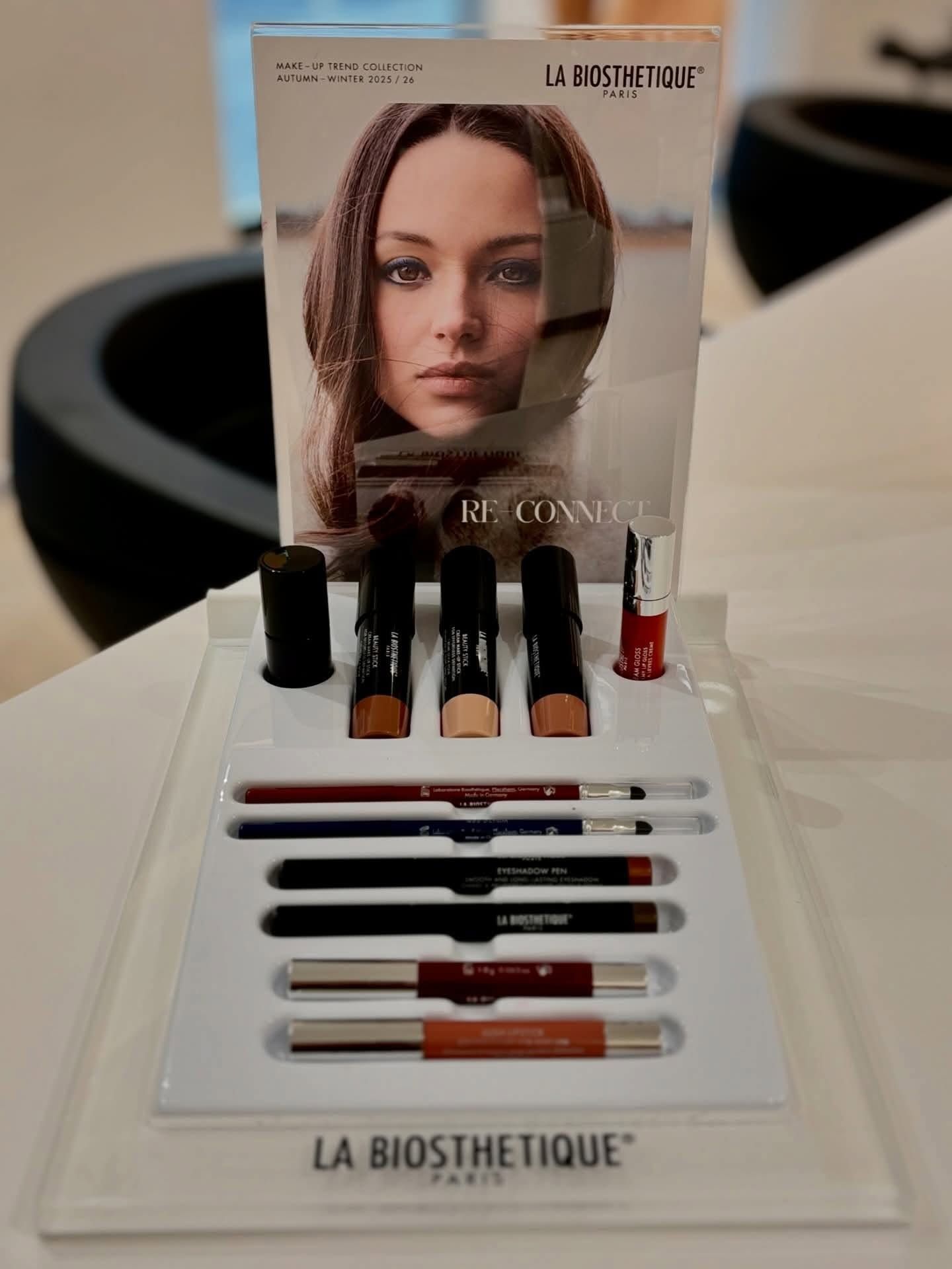 Présentoir de maquillage La Biosthetique avec des gloss, des crayons à lèvres et une affiche de mannequin en arrière-plan.