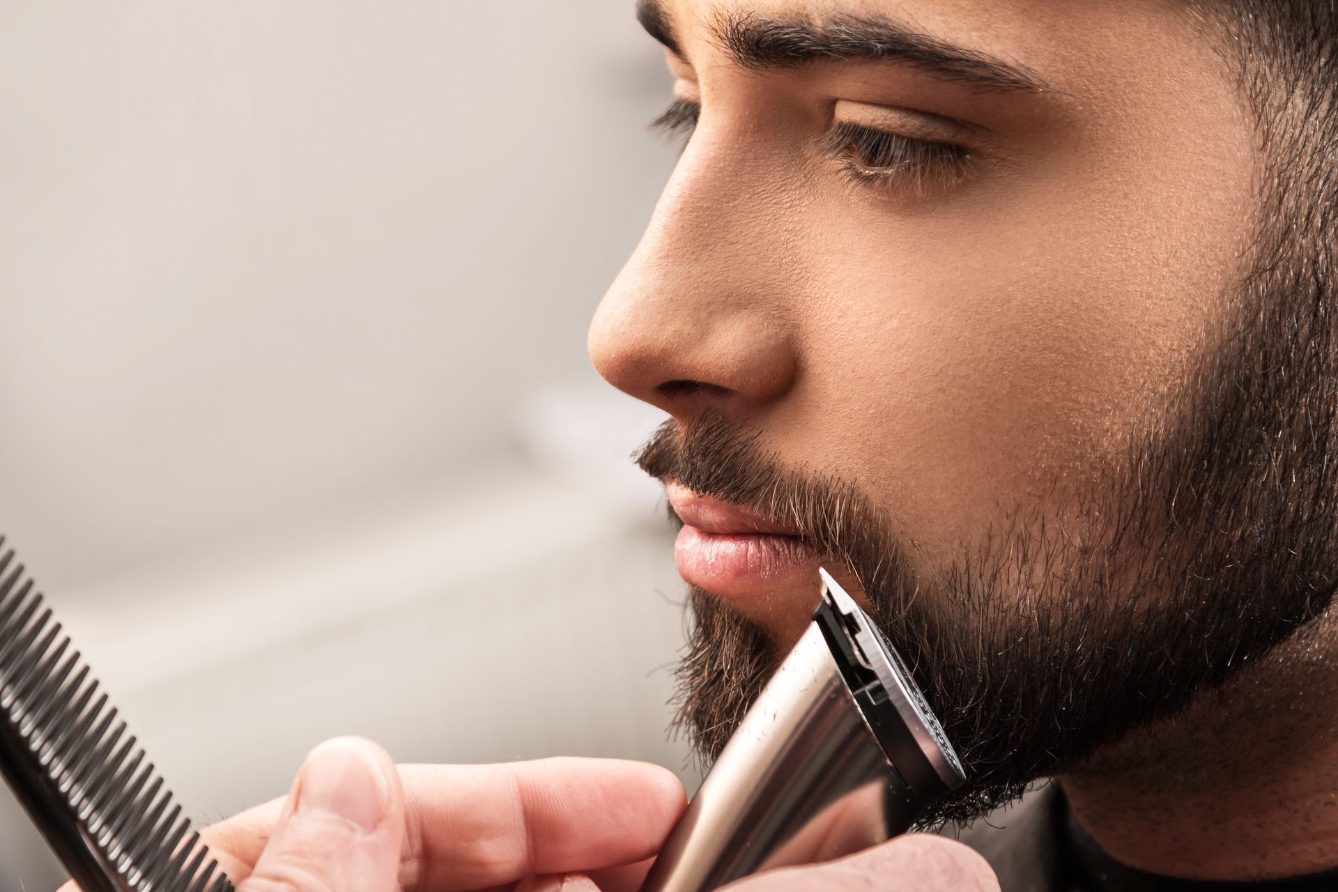 Un homme barbu se faisant tailler les poils du visage avec un rasoir électrique et un peigne.