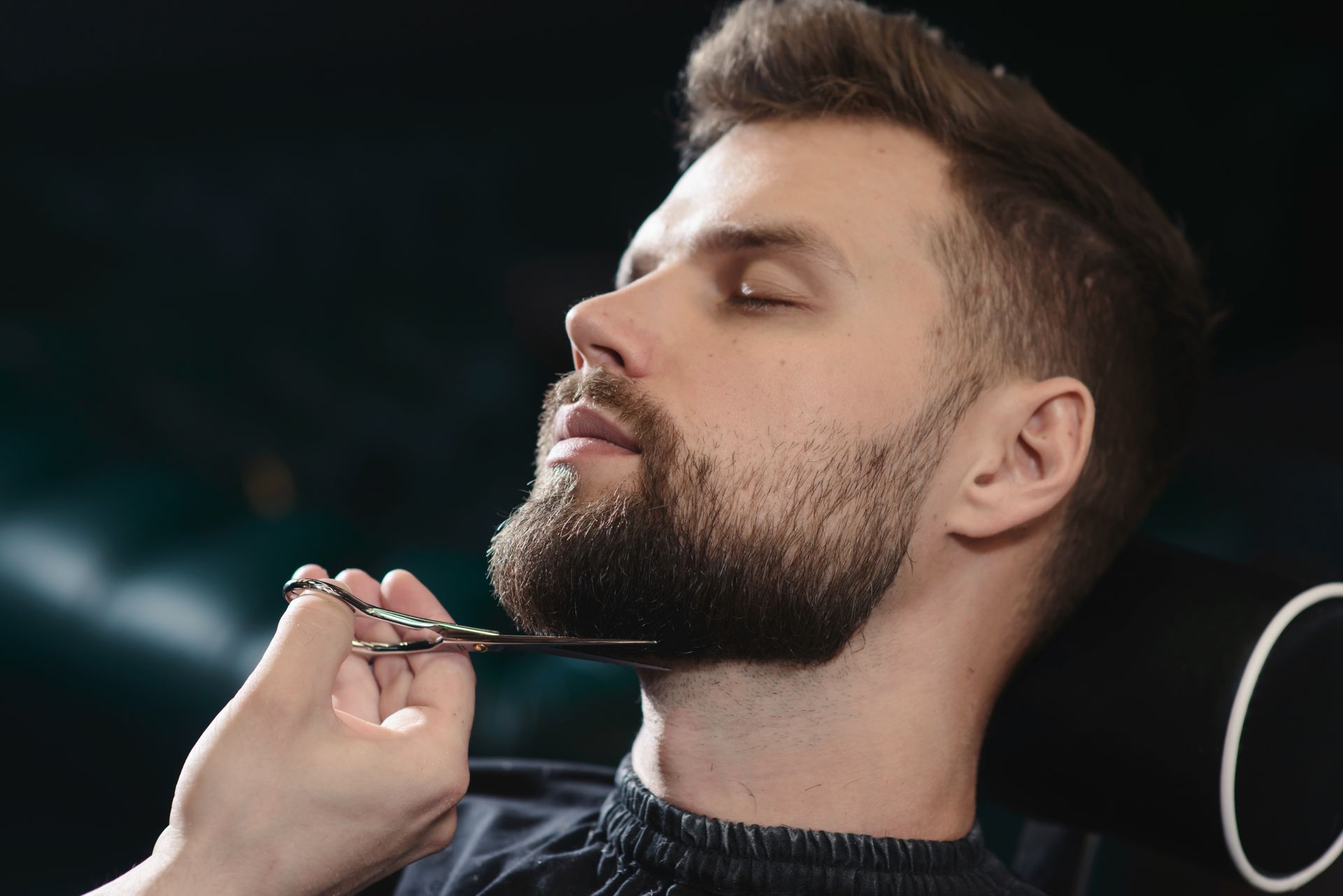 Un coiffeur taille la barbe d'un homme avec des ciseaux.