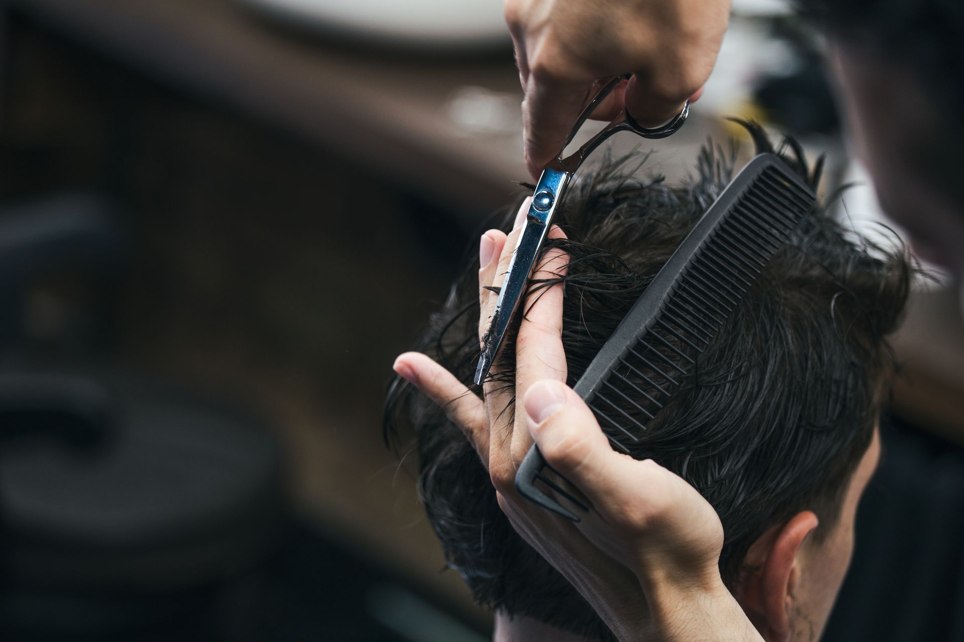 Coiffeuse coupant les cheveux foncés d'un client avec des ciseaux et un peigne.