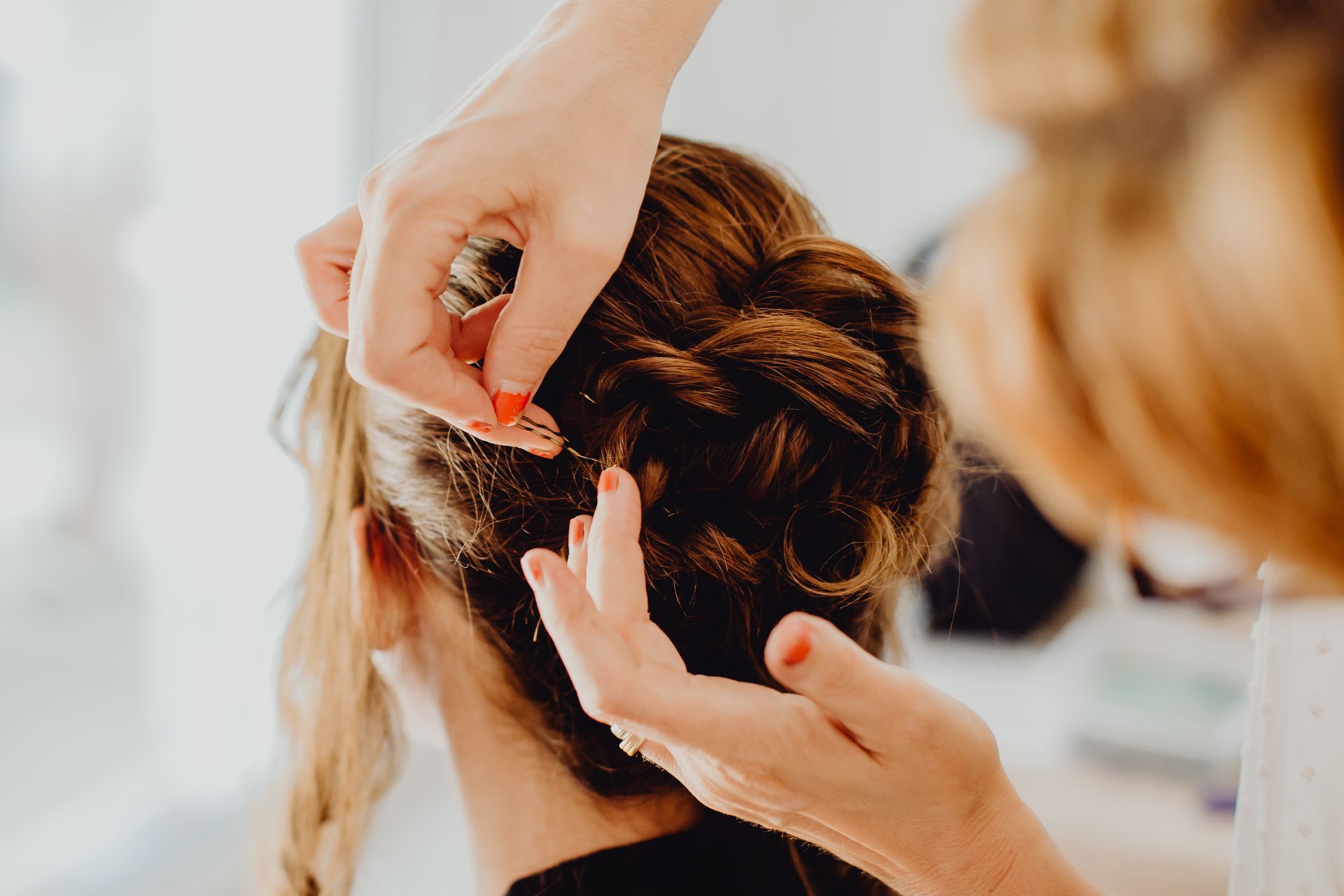 Des mains réalisent une coiffure tressée sur les cheveux d'une femme dans un salon de coiffure.