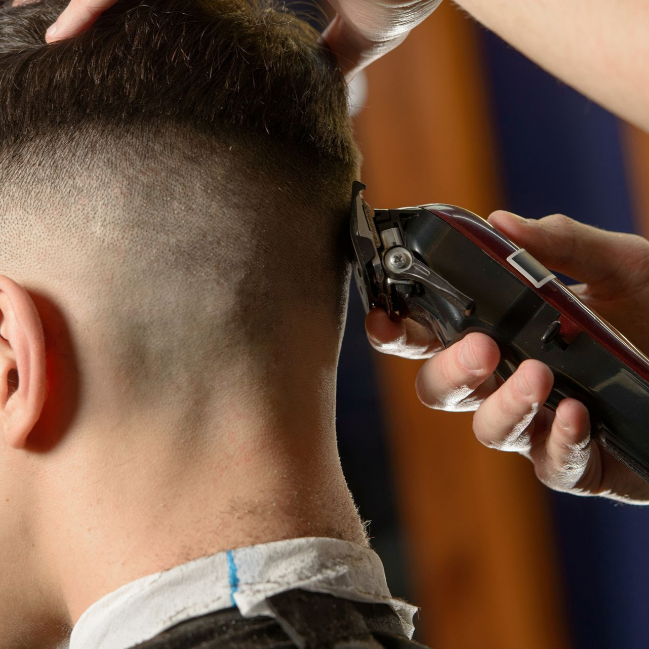 Un coiffeur taillant les cheveux d'un client homme avec une tondeuse électrique.