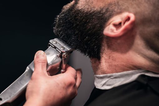 Un barbier taillant la barbe d'un homme avec une tondeuse électrique.