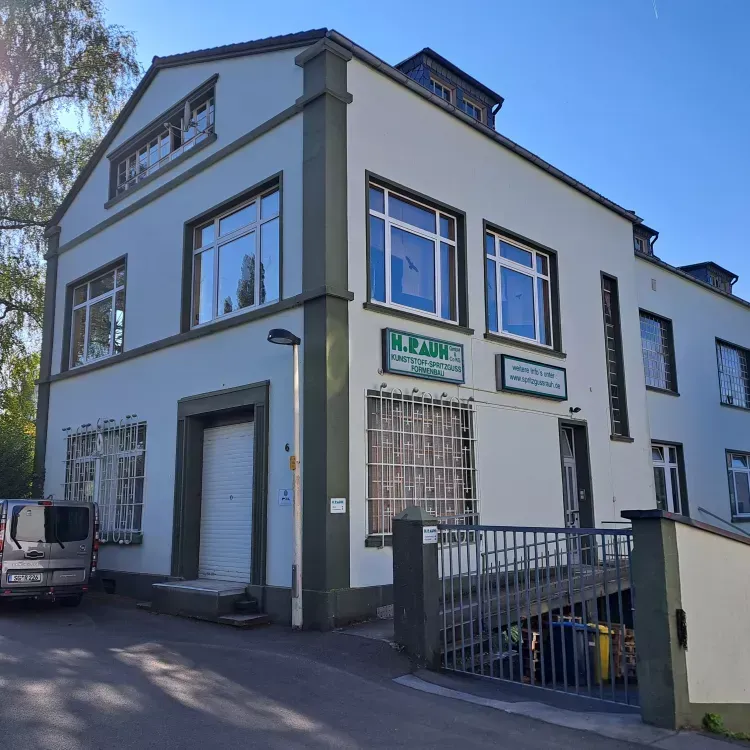 Zweistöckiges Gebäude mit weißen Wänden, grünen Zierelementen und mehreren Fenstern. Es trägt ein Schild mit der Aufschrift „H. AL-AMIN“ und hat einen Eingangsbereich mit Tor.