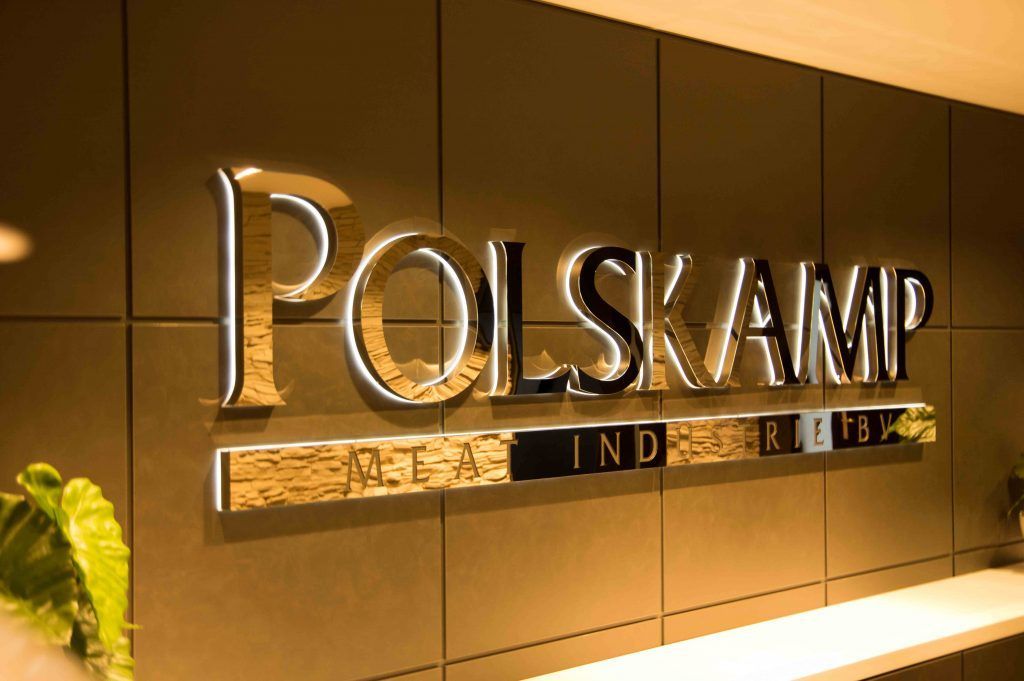 Polsamp-Schild an einer braunen Wand in einer warm beleuchteten Lobby, links daneben eine kleine Pflanze.