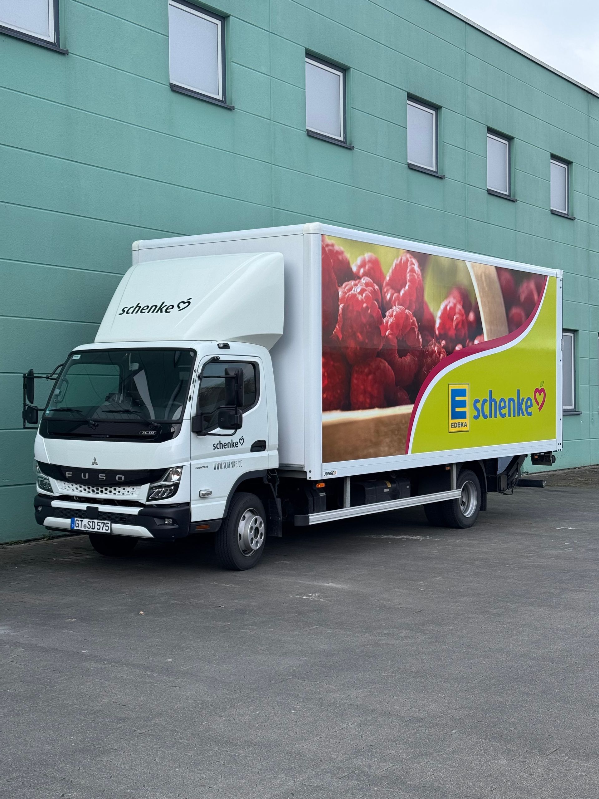 Weißer Lieferwagen mit Fruchtmotiv parkt neben einem grünen Industriegebäude