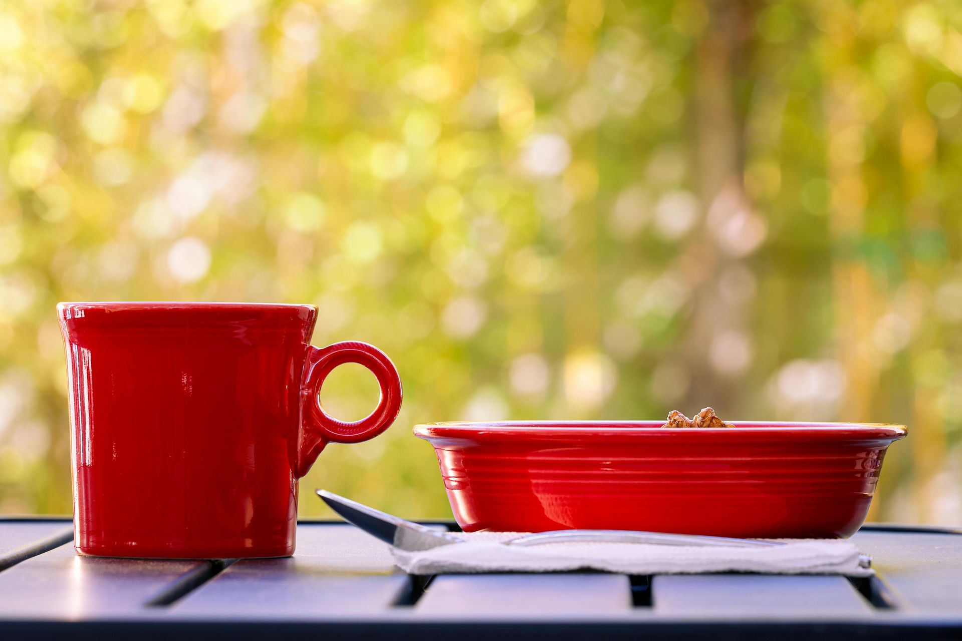 Red mug and red saucer on a tray against a blurred yellow-green outdoor background