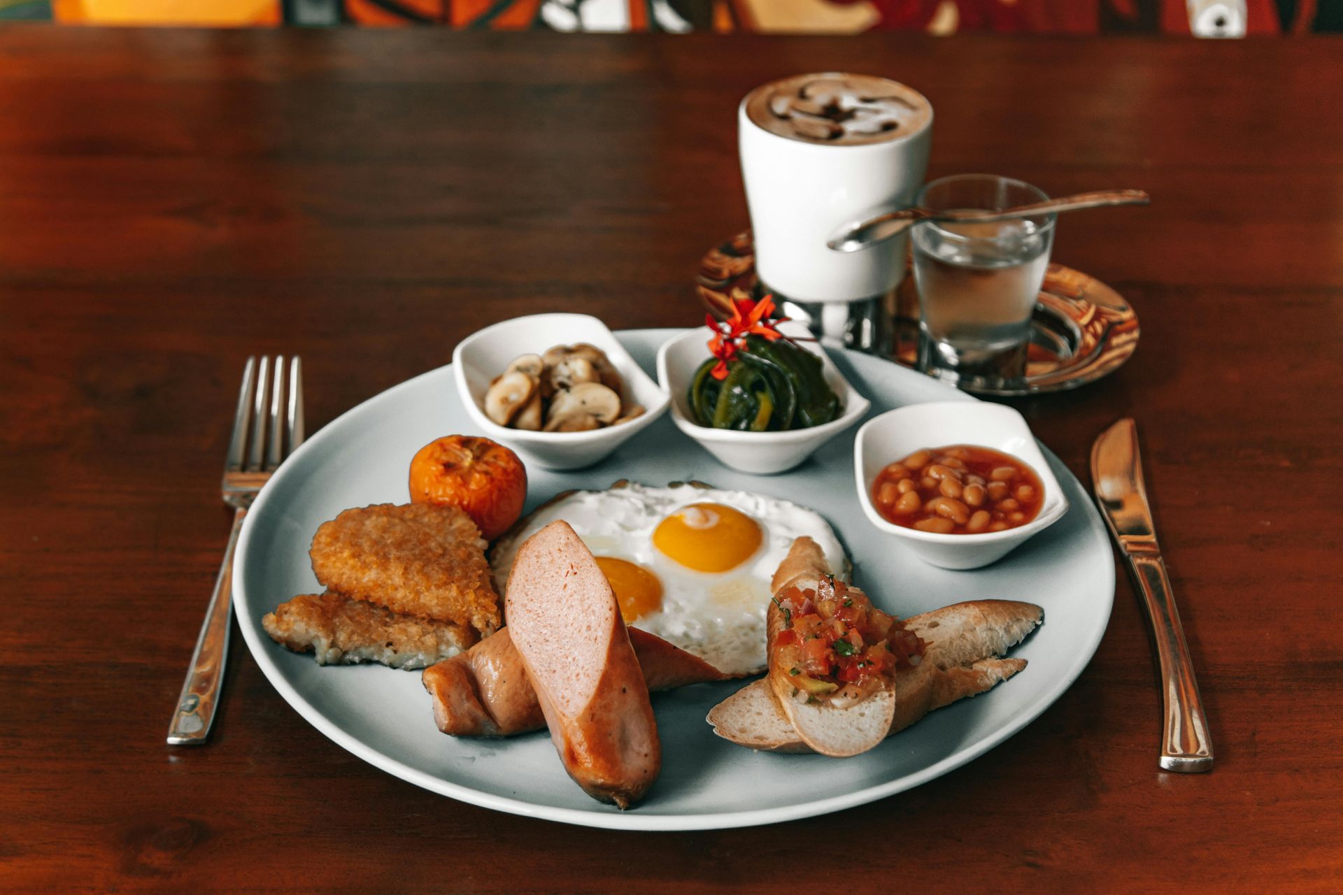 Breakfast plate with eggs, sausage, toast, potatoes, coffee, and jam on a wooden table