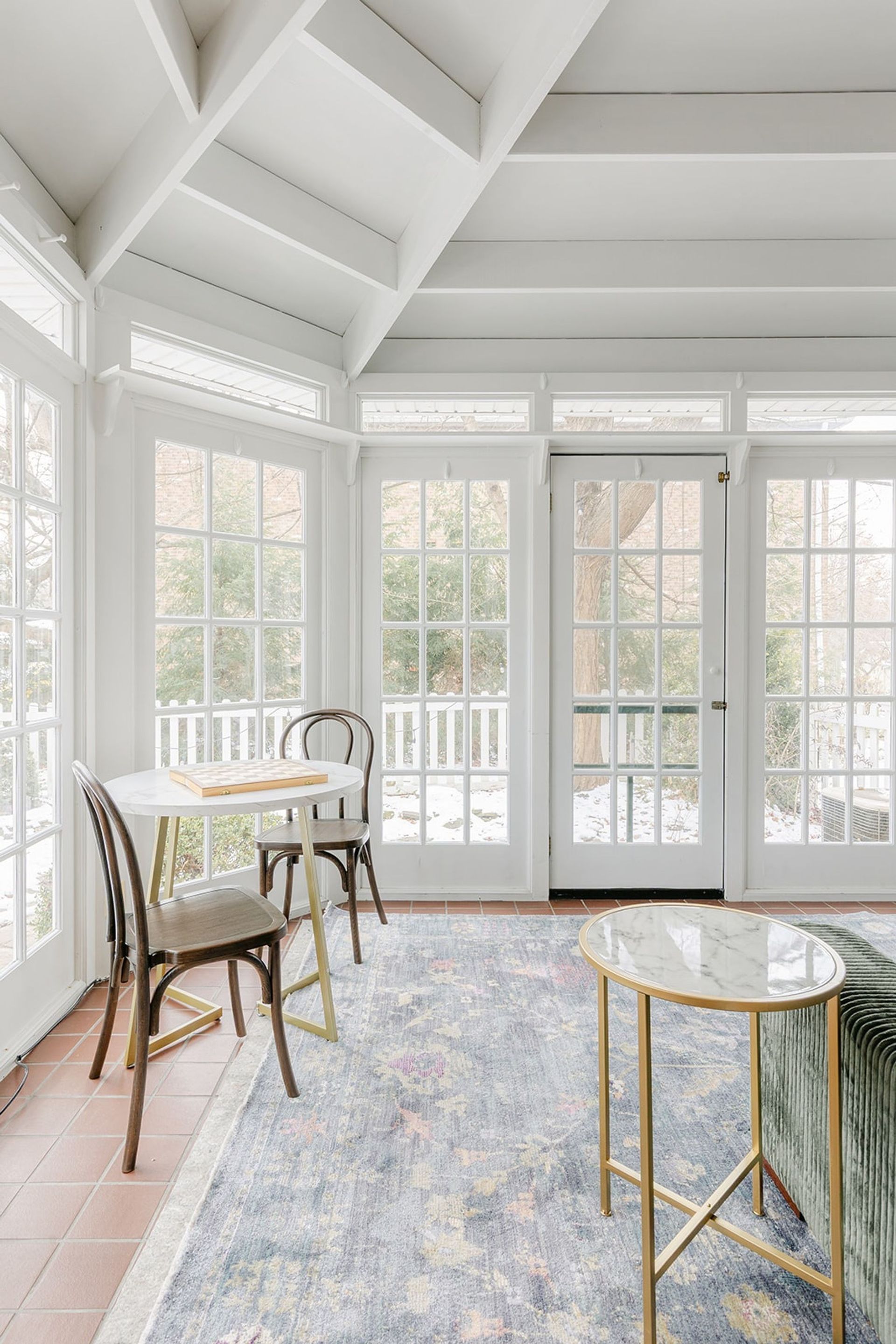Bright sunroom with large windows, white walls, wicker chairs, and a rug on wood floors