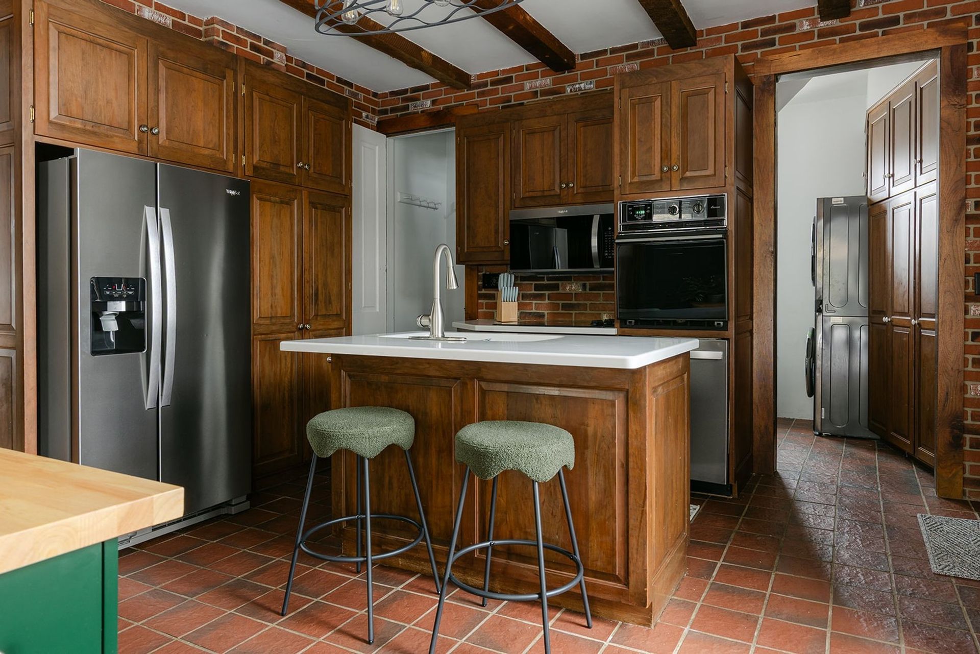Wood-paneled kitchen with stainless steel appliances, island, and two bar stools.