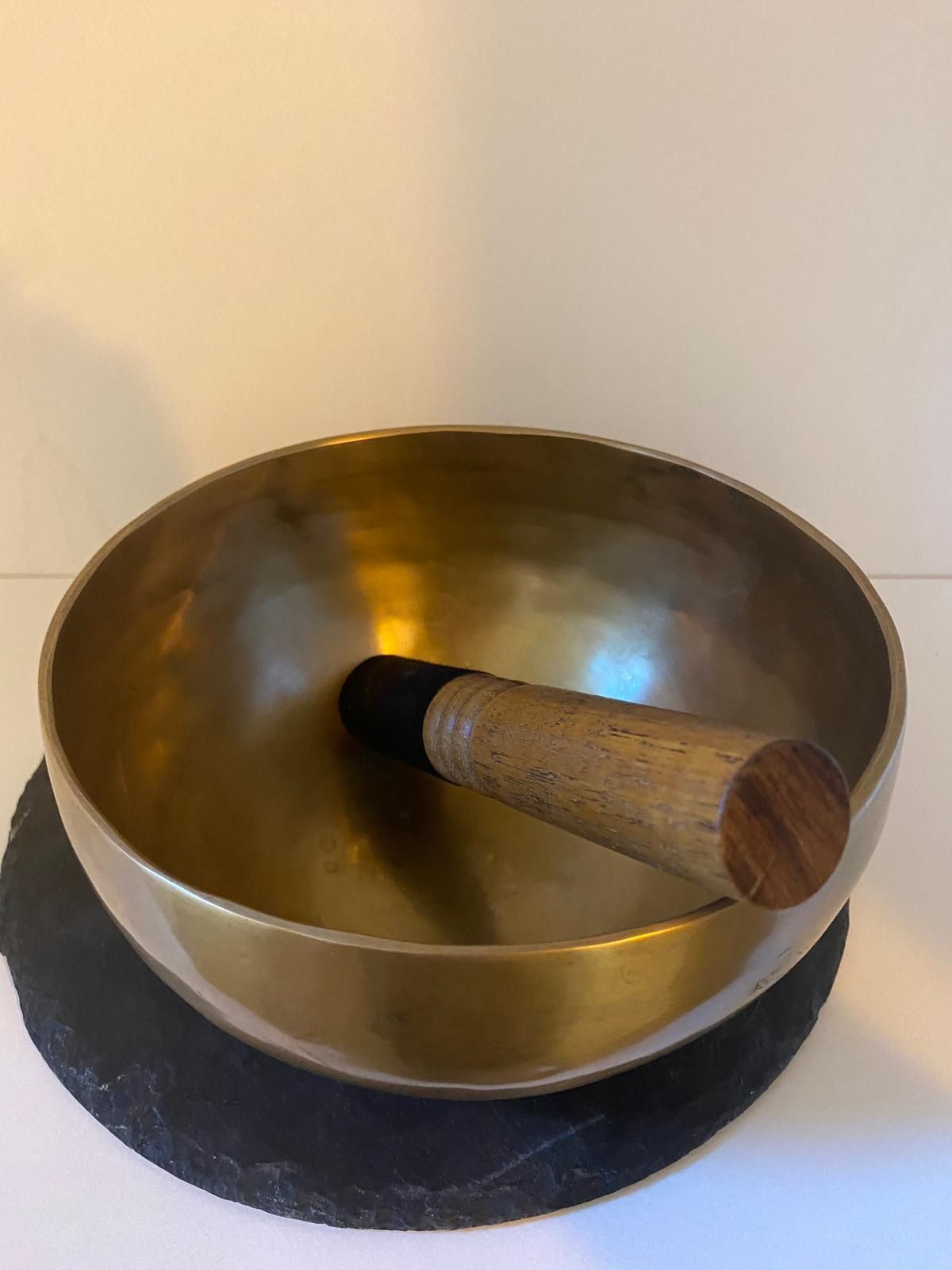 Un cuenco de latón con mango de madera reposa sobre una estera de pizarra.