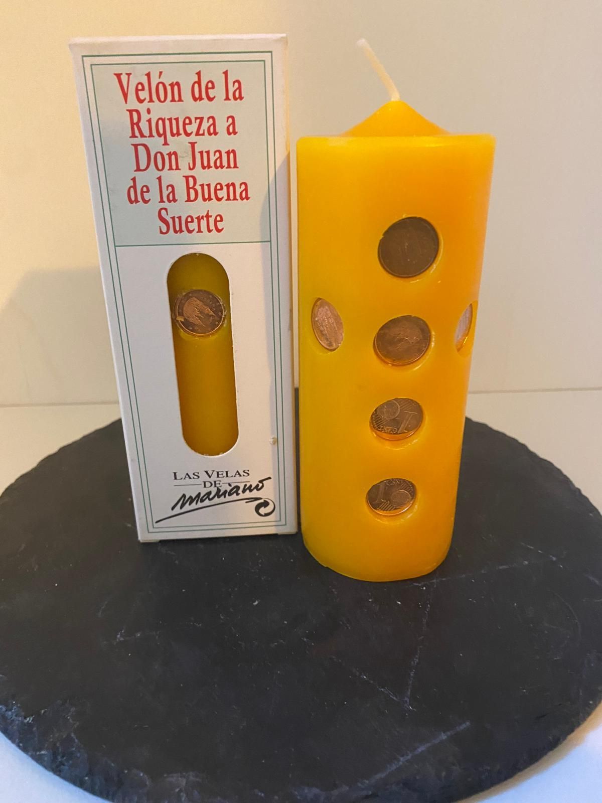 A yellow candle sits next to a box that says velon de la riqueza a don juan de la buena suerte