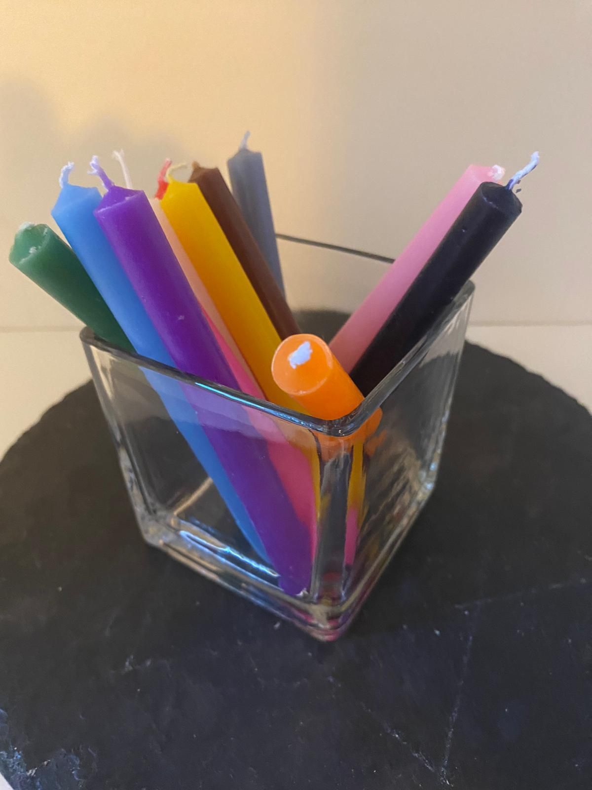 Un recipiente de vidrio lleno de muchas velas de diferentes colores.