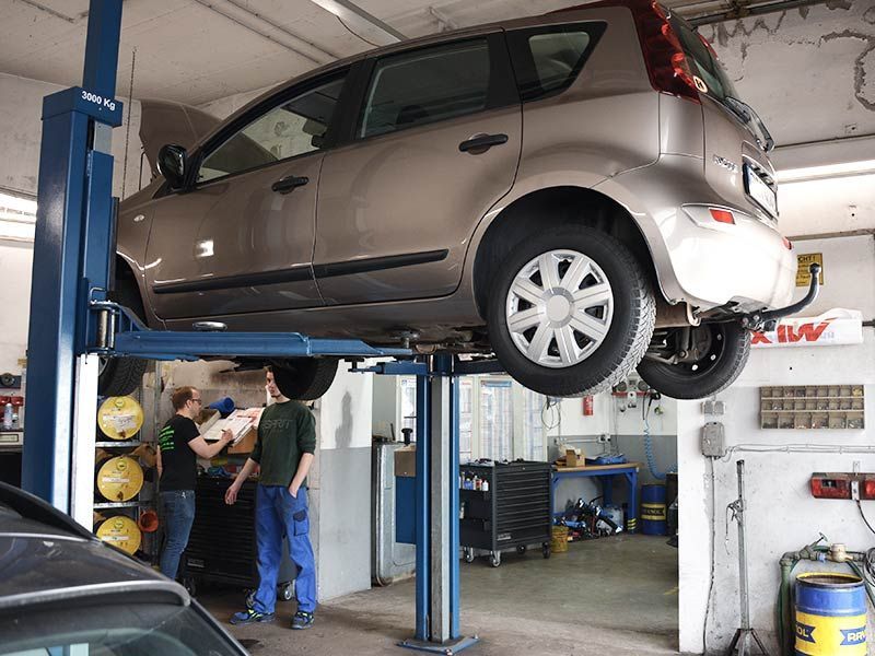Ein Auto auf einer Hebebühne in einer Garage mit einem Tuw-Schild an der Wand