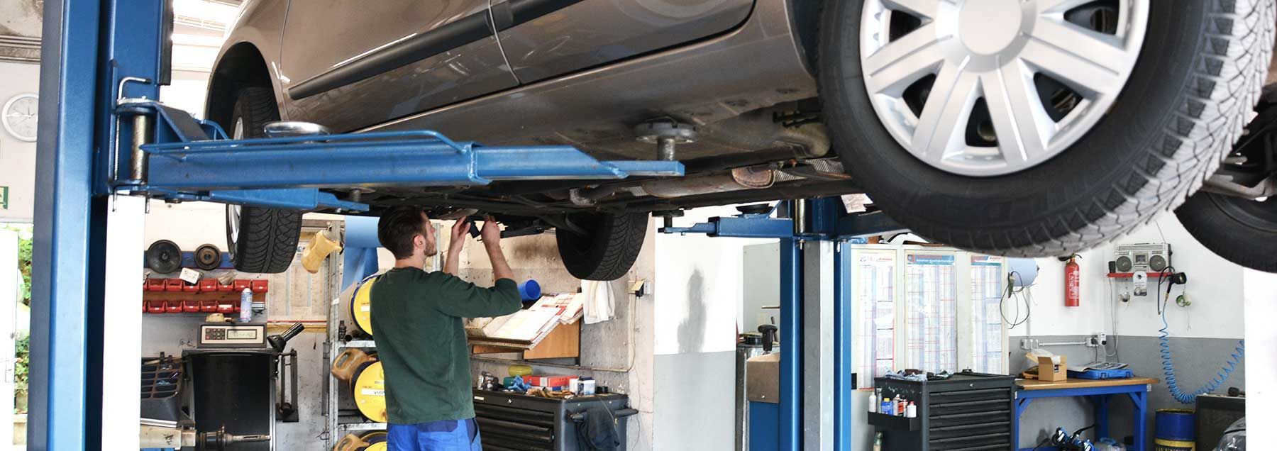 Ein Mann arbeitet unter einem Auto auf einer Hebebühne in einer Garage