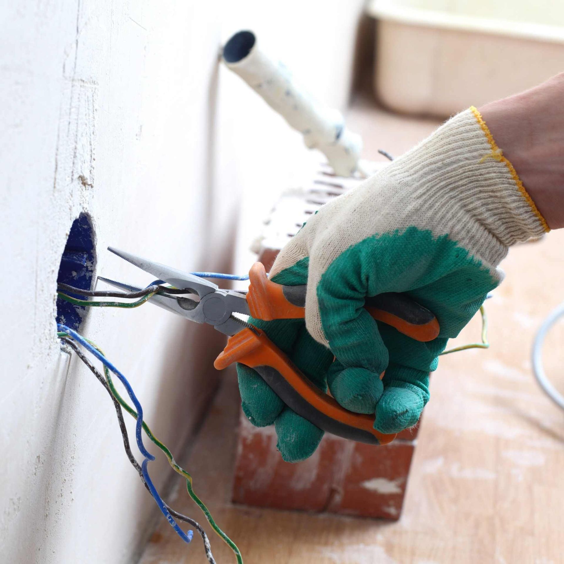 Persona que usa un guante de trabajo y utiliza alicates para trabajar con cables eléctricos en una pared.