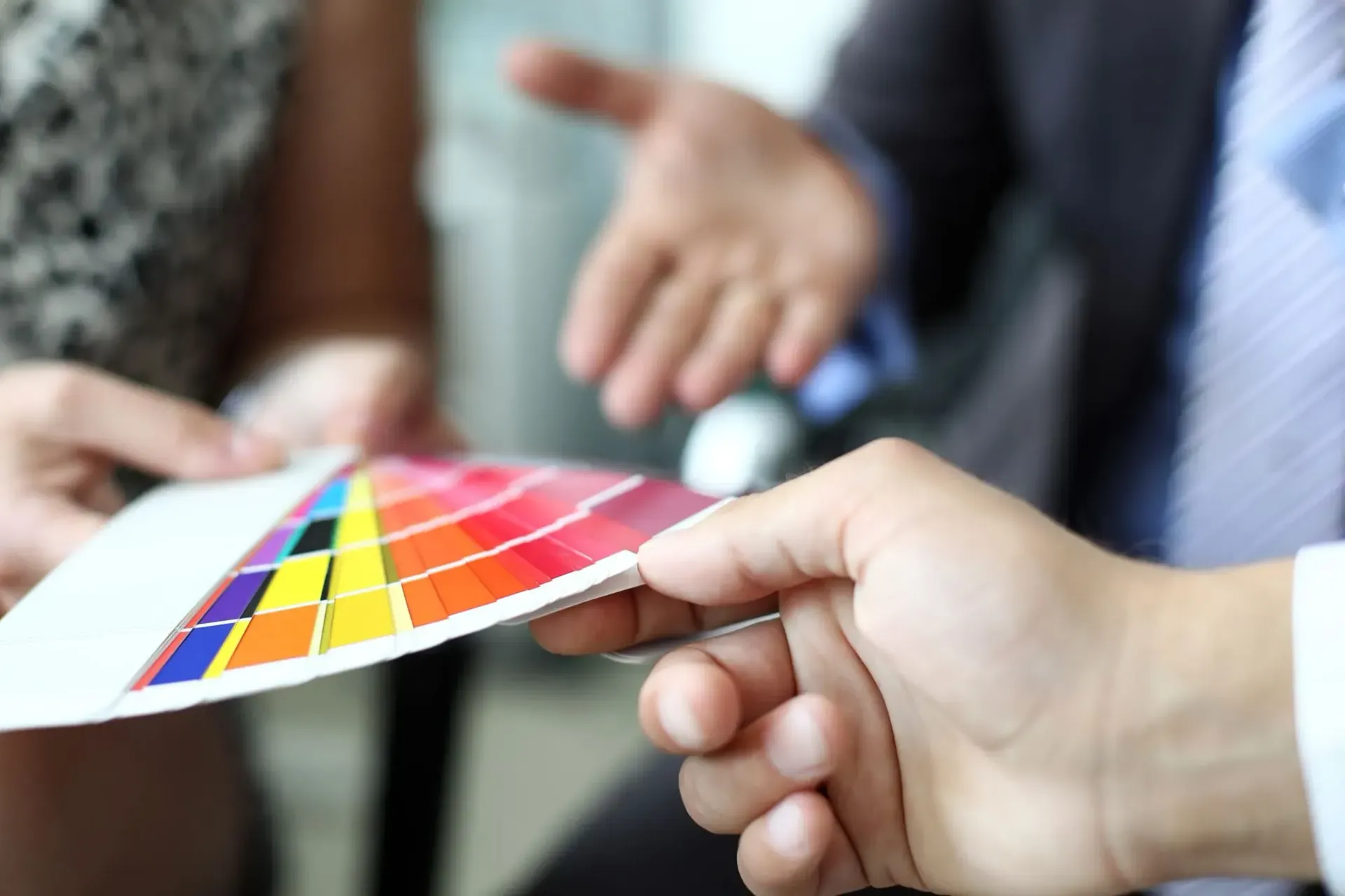 Manos sosteniendo y señalando una paleta de colores, discutiendo opciones con otra persona.